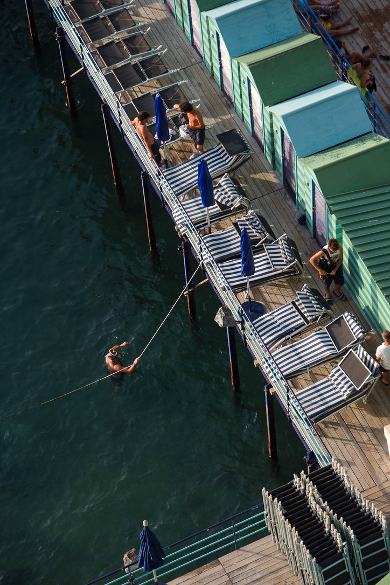 a man holding a rope in the water below lounge chairs on a pier in Sorrento
